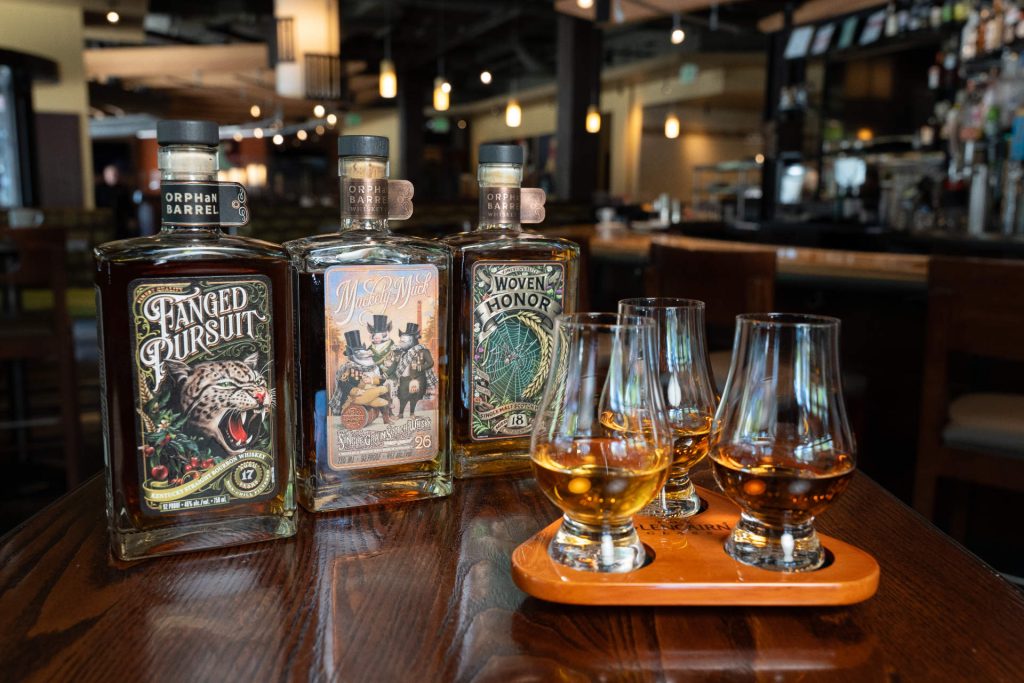 Orphan Barrel whiskey bottles with a flight of three whiskeys in tasting glasses